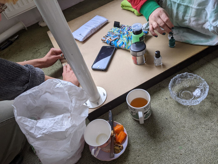 a view of tea and snacks on the floor and the hands of two people busy with applying nailpolish