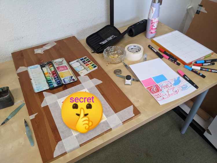 a desk strewn with watercolours and paint markers and sticker sheets